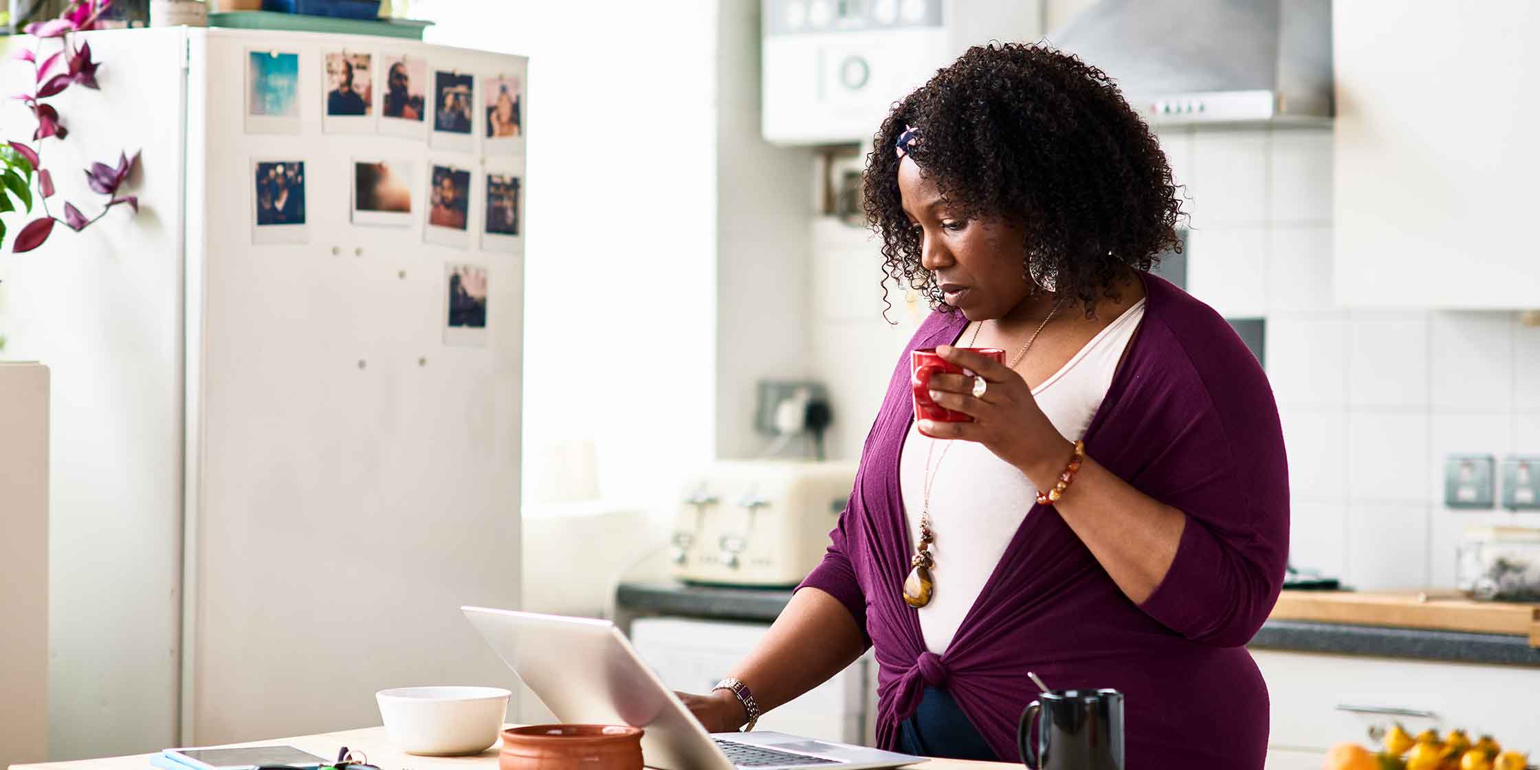 A person stands at their kitchen counter and reads on their laptop about the Fair Credit Billing Act.