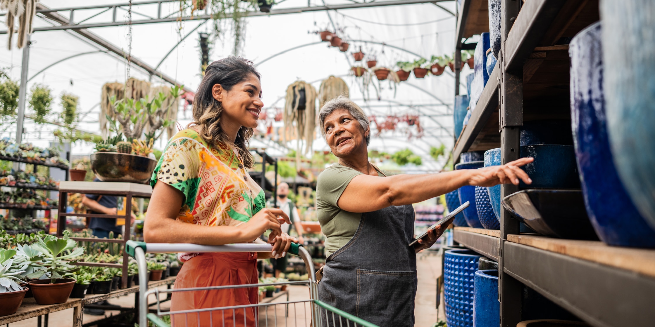 A person shops at a garden center, and an employee helps them choose a ceramic pot.