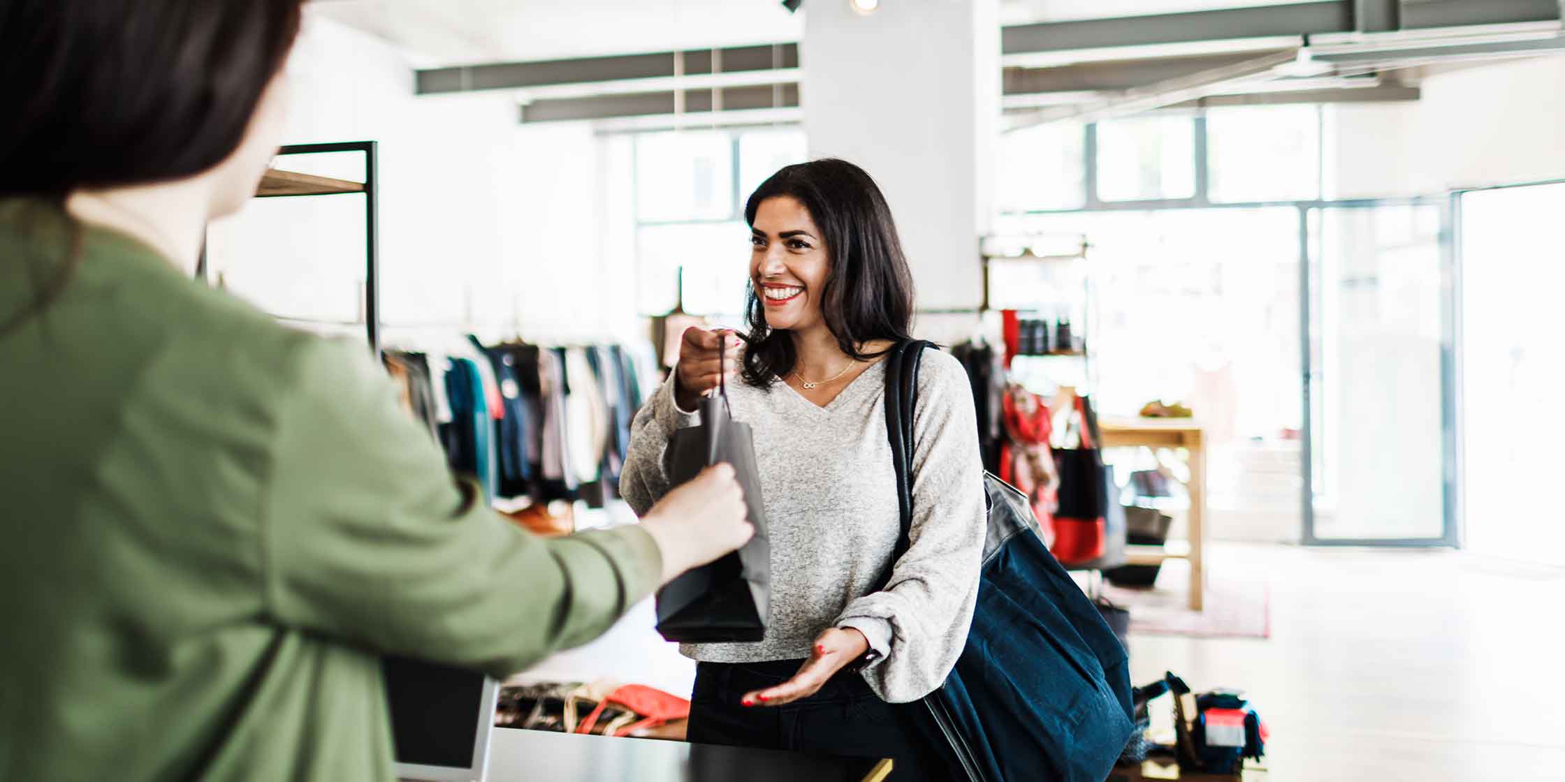 An associate in a clothes boutique hands a credit card back to their customer holding their purchase in a bag.