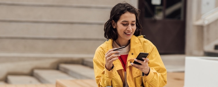 A smiling person looking at their credit card balance on their phone.