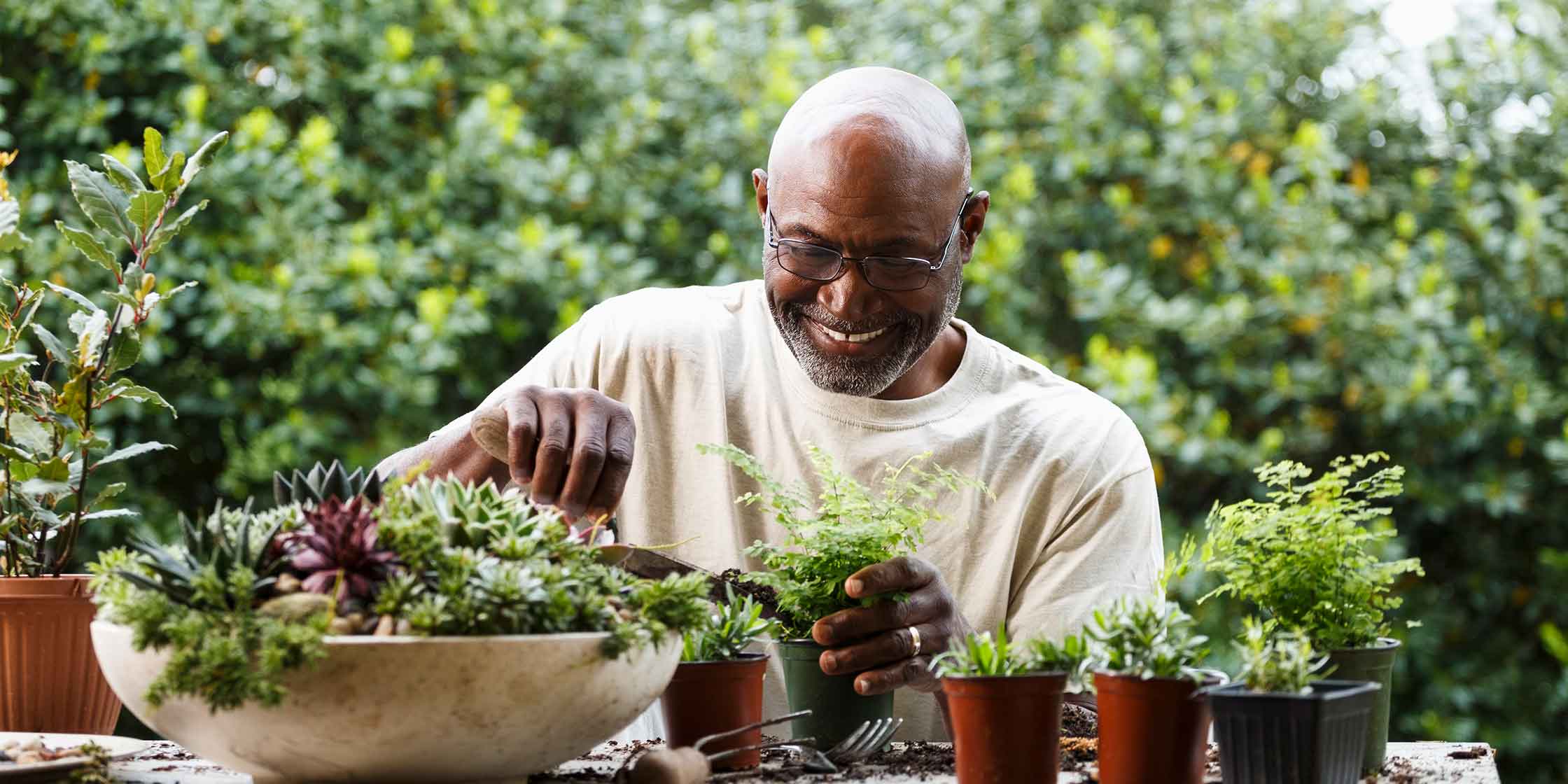A man smiles as he pots a number of small plants outside.