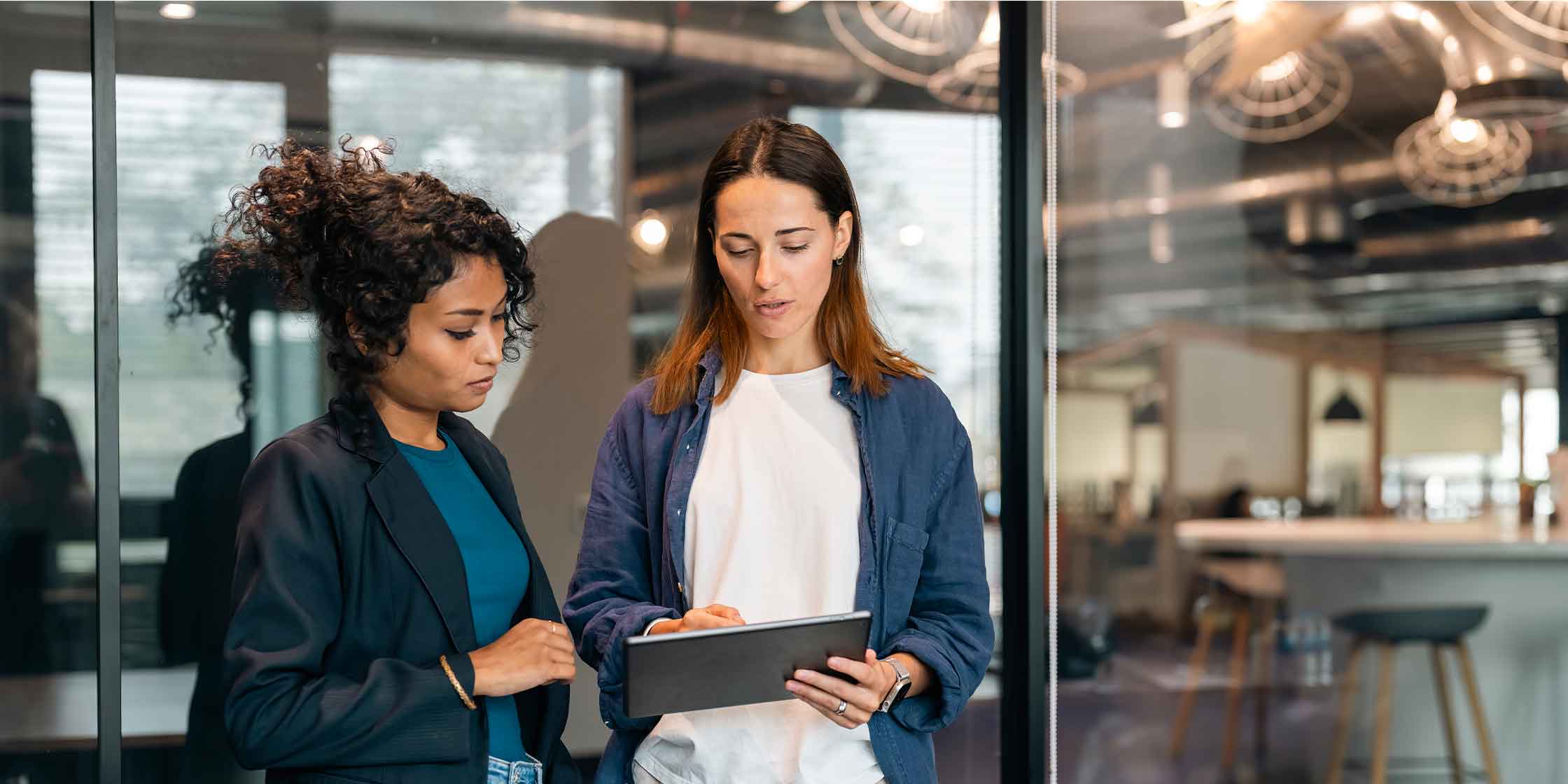 Two people standing next to each other and looking at a tablet outside a conference room.