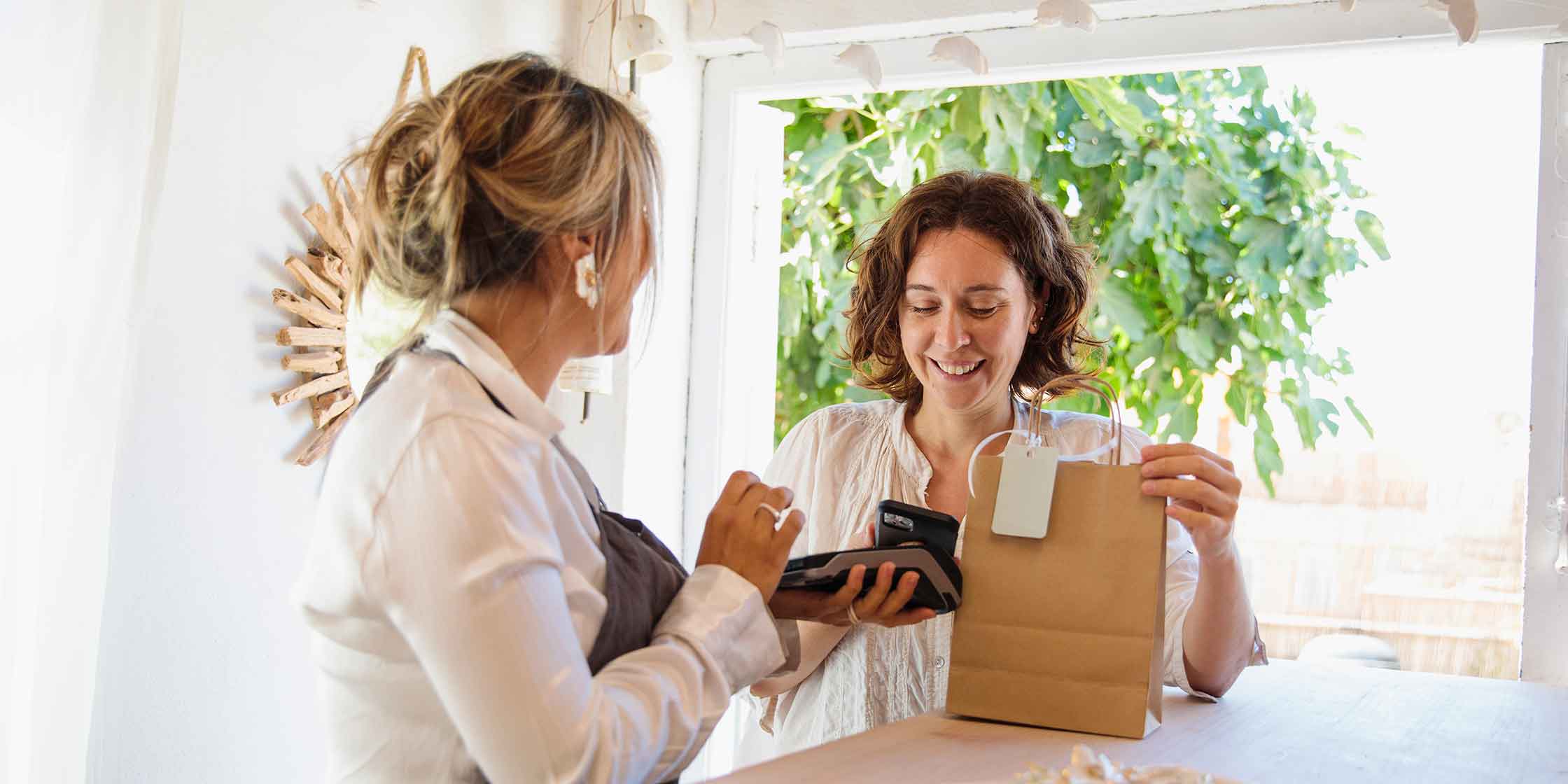 A smiling person holding a gift bag while using their phone to pay for their purchase.