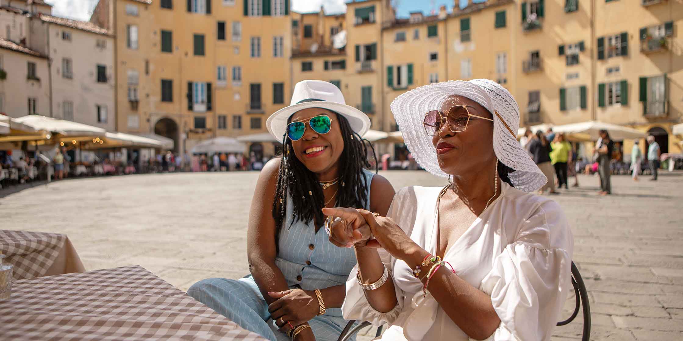 Two people sitting at a café in a sunny town square.