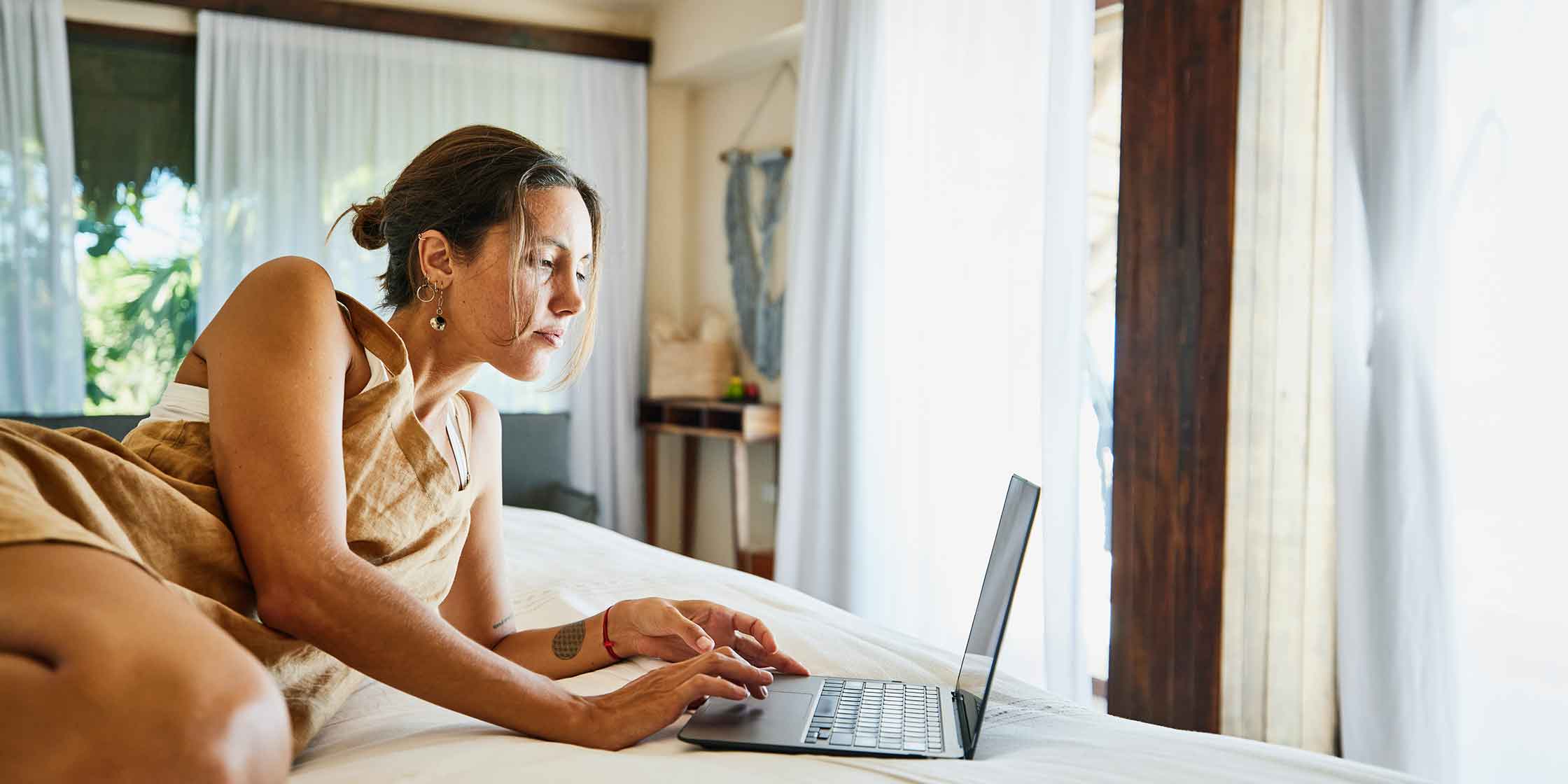 A person lounging on their bed while using their laptop to check their credit score.