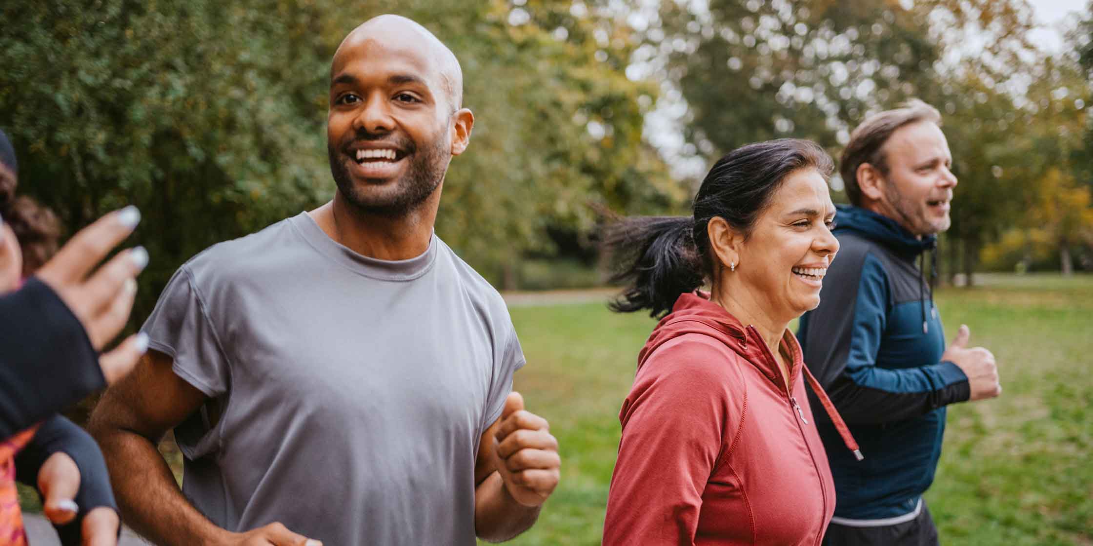 A small group of runners smiling as they jog through a park.