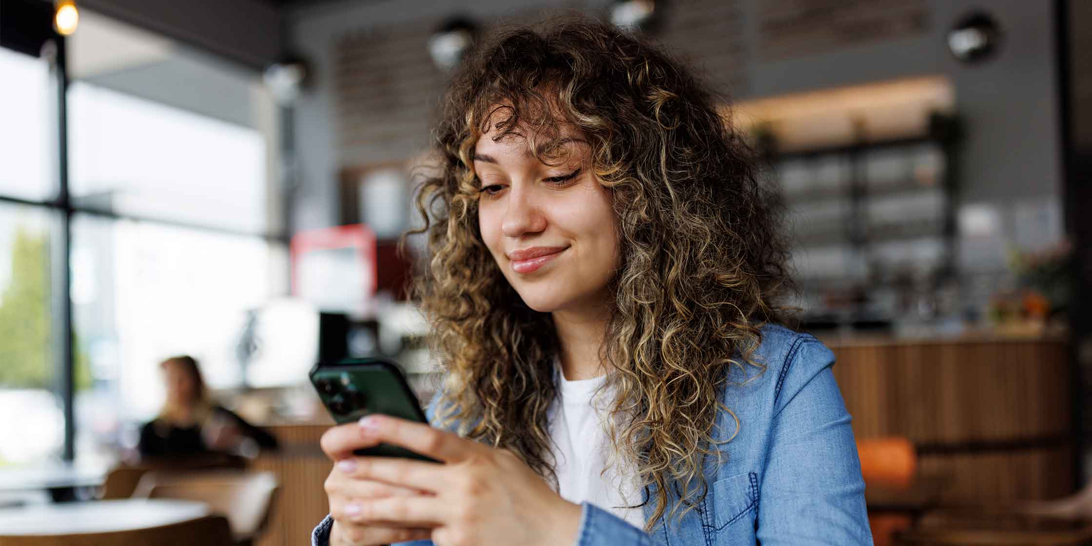 A smiling person looking at their smartphone while sitting in a restaurant.