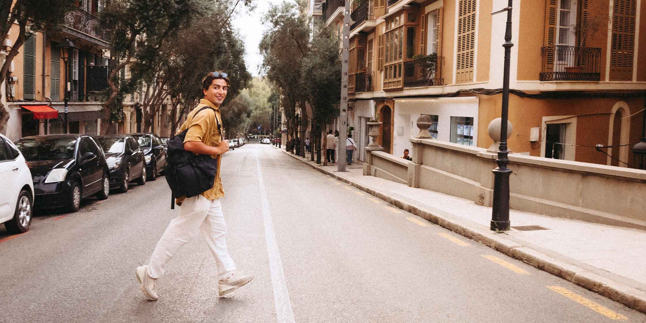 A smiling person carrying a backpack crosses the street in Spain.