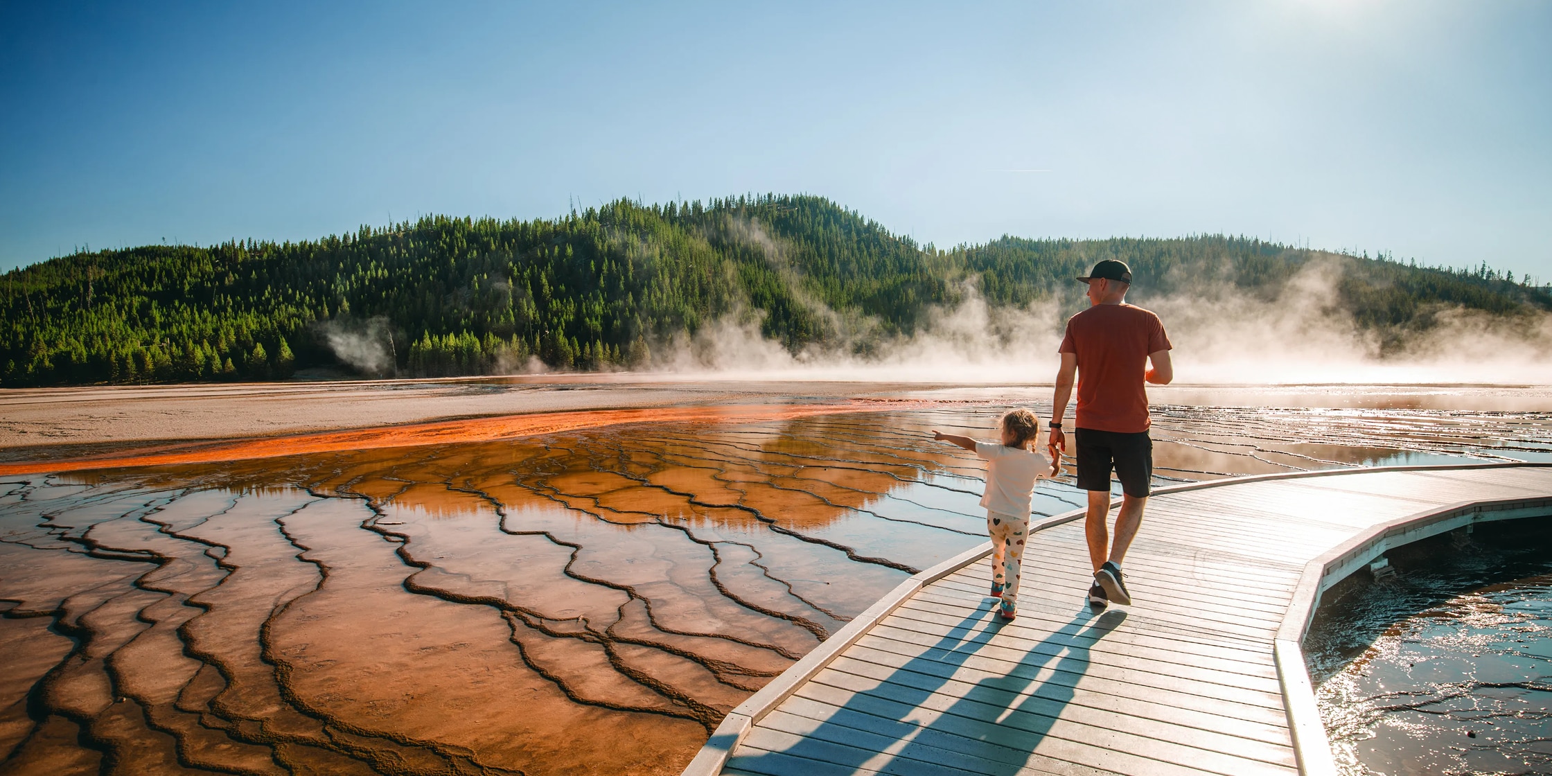 A parent and child walking along the boardwalk at Midway Geyser Basin in Yellowstone National Park.