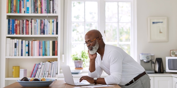 A person looking at their laptop while standing in their kitchen.