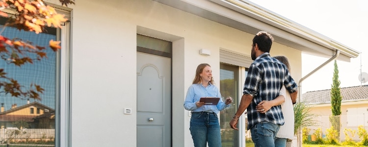 A couple talks with a real estate agent about closing costs while standing outside of a home.