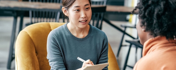 A woman sits opposite a job candidate and takes notes with a pen and paper.