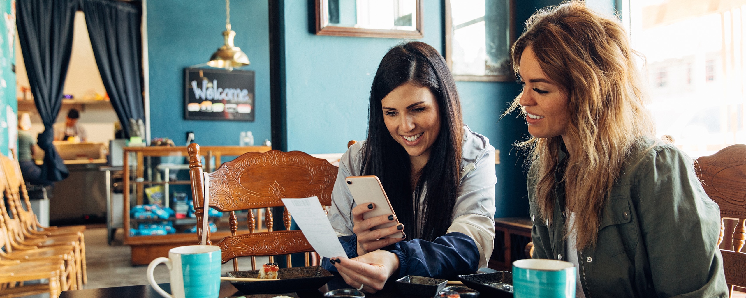 Two friends sit at a coffee shop and figure out how to split the bill by using a money transfer service.
