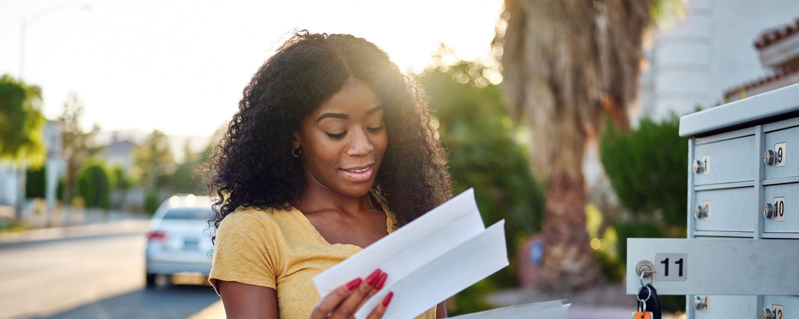 A person opens a mailbox and looks at a money order they received in the mail.