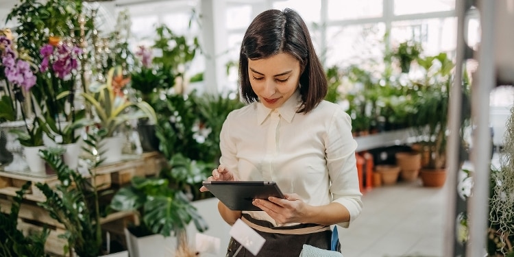 A person in a greenhouse looking at a tablet.