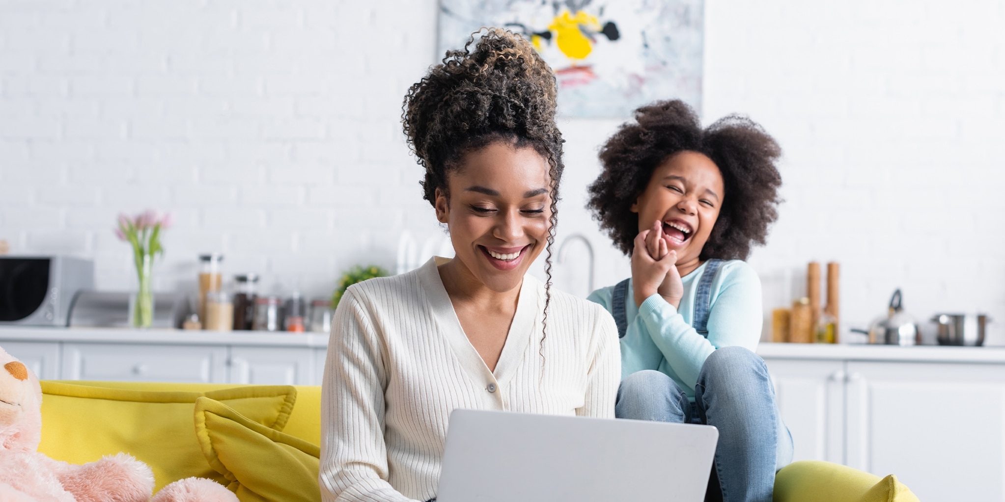 A parent and child laughing together while looking at a laptop.