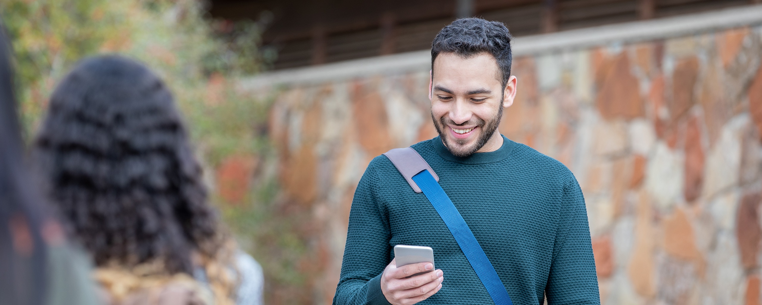 A student wearing a messenger bag checks his credit score on his phone.