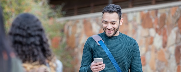 A student wearing a messenger bag checks his credit score on his phone.