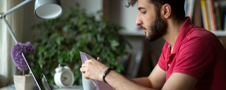 A person sits at a desk with a laptop on it while holding something in his hand.