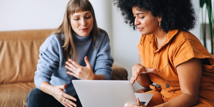 Two people sit and talk about compound interest while looking at a laptop screen.
