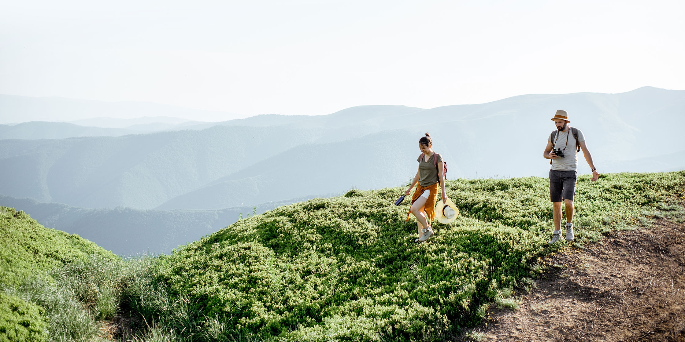 Two people hiking on top of a mountain in warm, sunny weather.