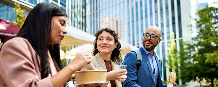 Three work colleagues eating and drinking together outside in a city.