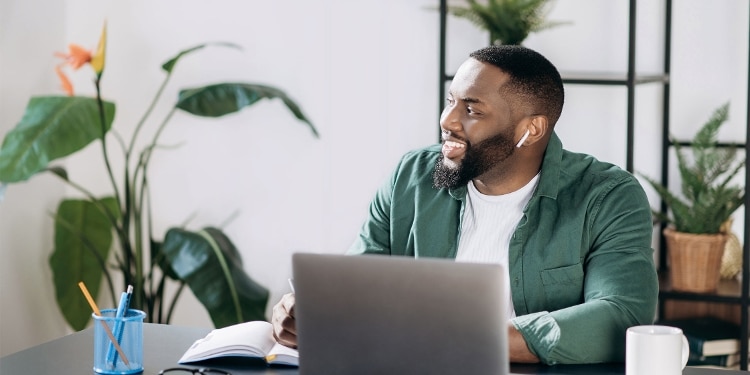 A man using his laptop to apply for a credit card at a desk with plants and office supplies around him.