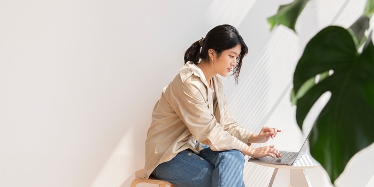 A person sitting in a bright room while using their laptop.