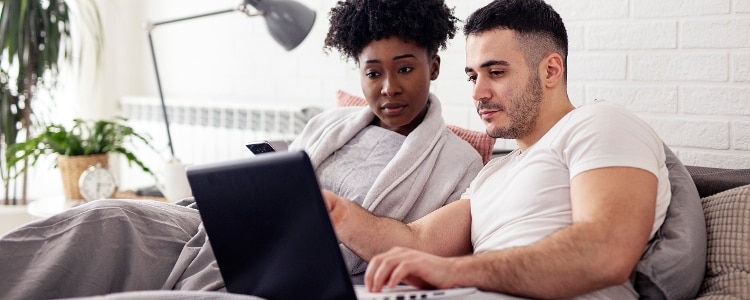 Two people sitting on a couch look at a screen together.