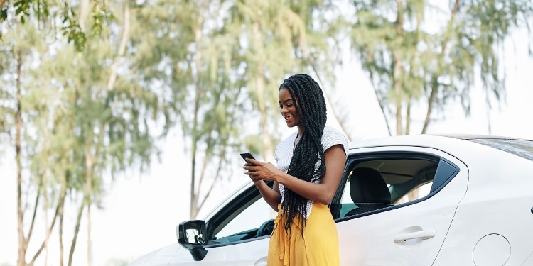 A person standing by their car researching credit card rental car insurance on their phone.