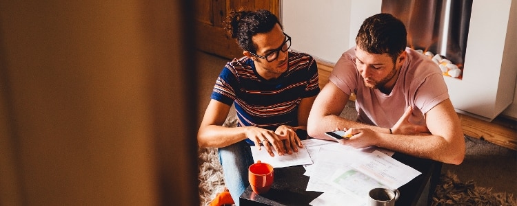 Two people sit on the floor while looking at papers on a table.