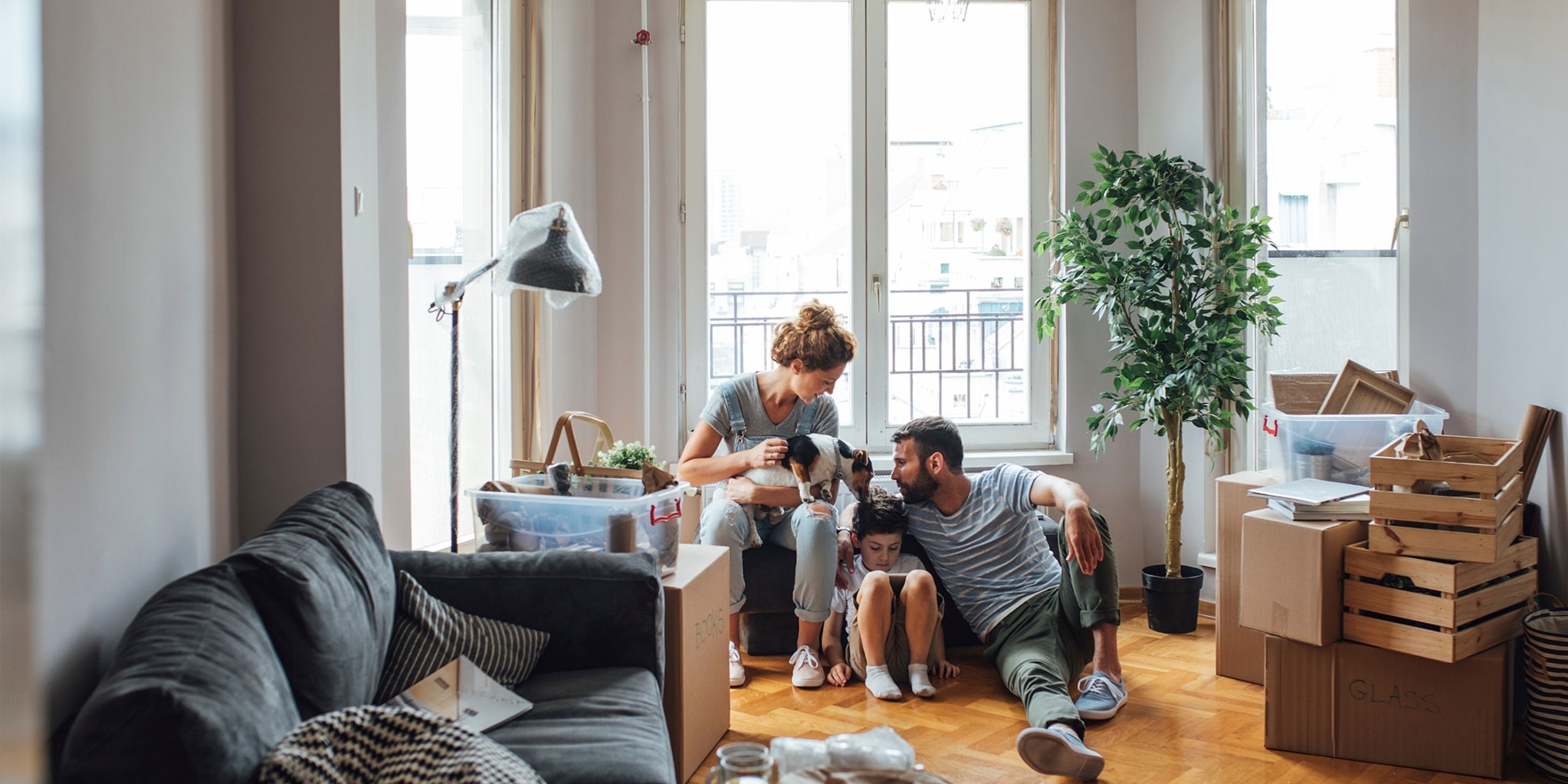 Two parents, a child and a dog surrounded by boxes in their new apartment.