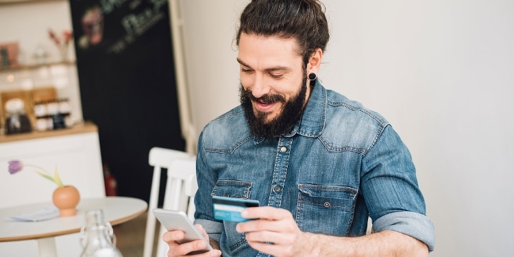 A smiling person looks at their cellphone while holding their credit card.
