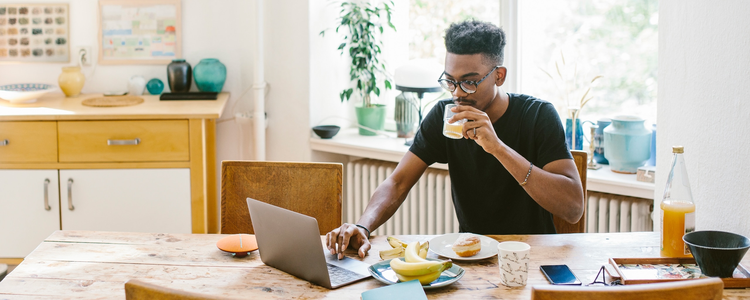 A person sits at a table while drinking juice and using a laptop.