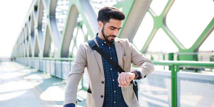 A smiling person checks their watch while walking across a bridge.