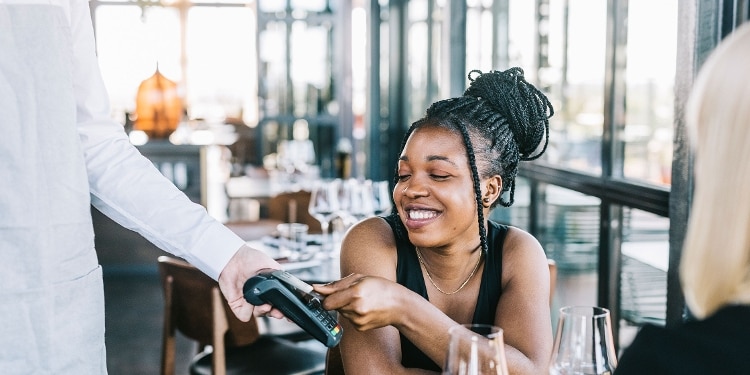 A smiling person pays for their restaurant meal using a cash back credit card.