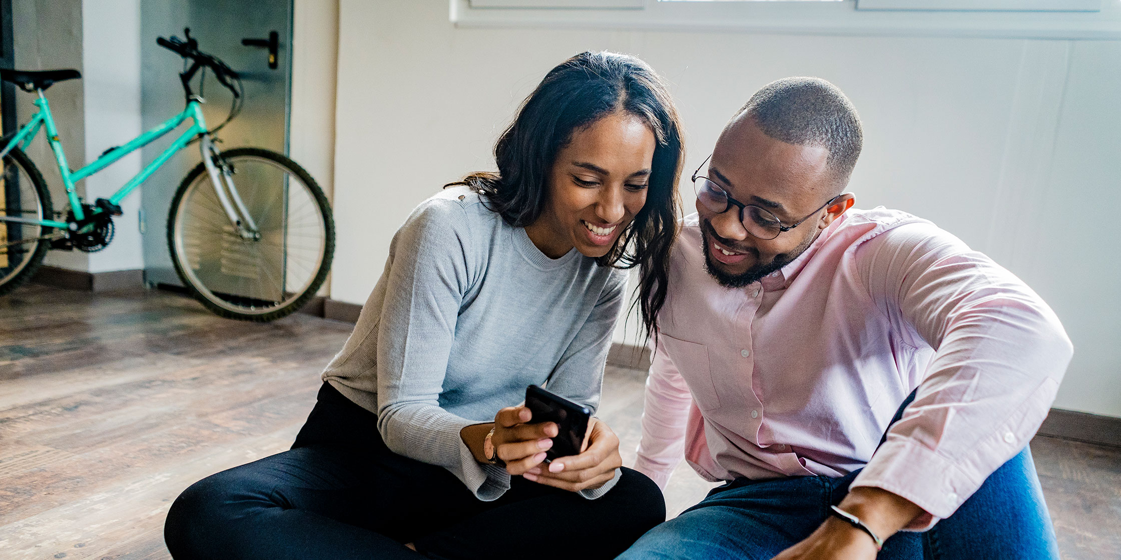 Two people sitting on the floor look at FICO scores on a cellphone screen.