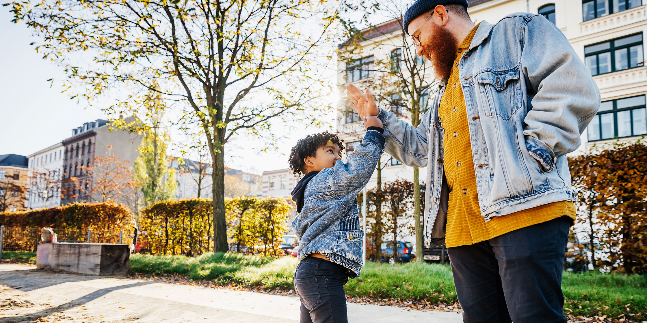 A father and son in denim jackets high-fiving outside.