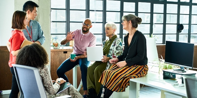 A group of people sit and stand in a circle in an office.