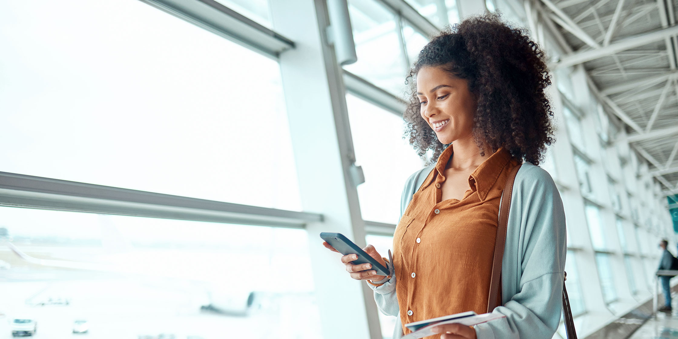 A smiling person looking at their Known Traveler Number on a mobile device while at the airport.