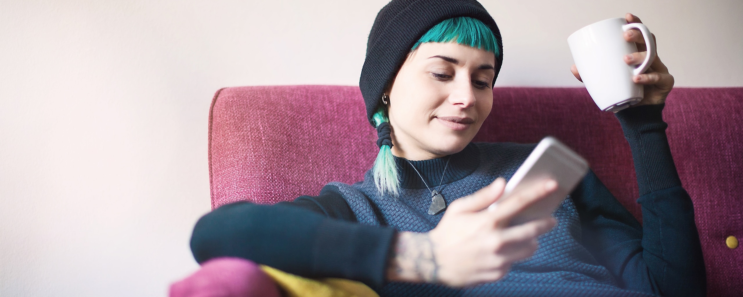 A person sits in a chair and looks at their phone while holding a mug.