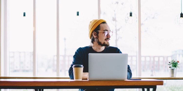 A person sits at a table while in front of a laptop and searches about overdrafts.