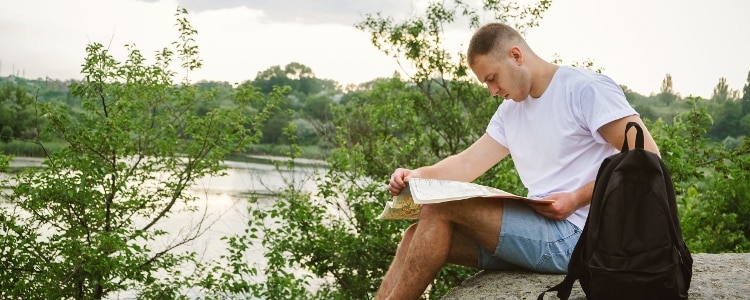 Person looking at a map while sitting on a rock overlooking a river.