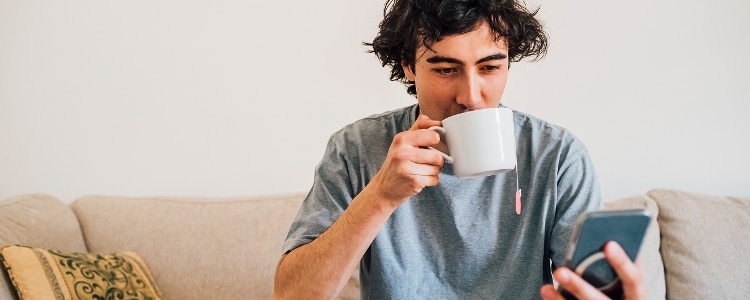 A person drinks a cup of tea while looking at their phone.