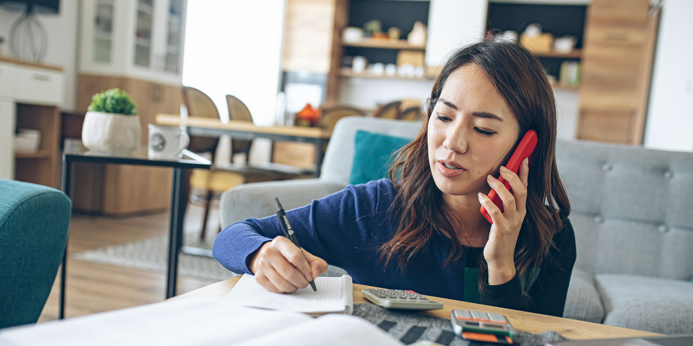 A person talks on the phone while using a pen and paper to take notes.