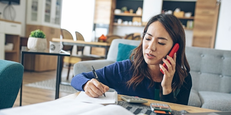 A person talks on the phone while using a pen and paper to take notes.