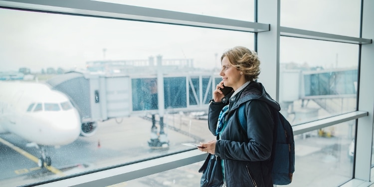 Airport traveler makes a call while looking through the window at a plane on the runway.