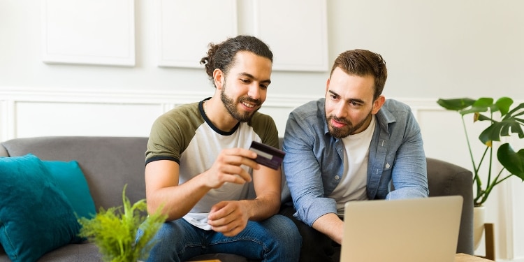 Two people sit on a couch looking at a credit card number together.