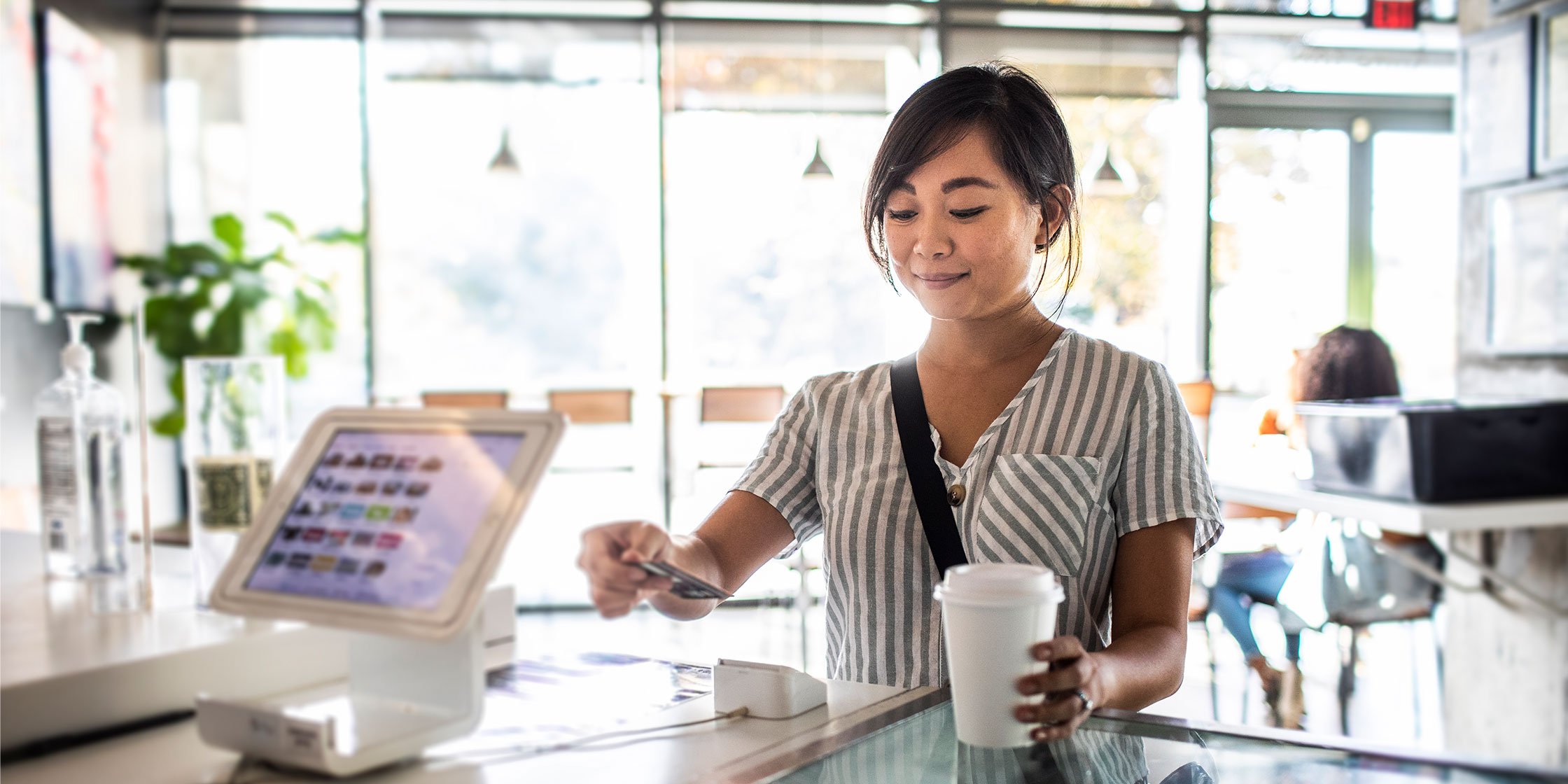 A person at the counter in a cafe uses a card to buy coffee.
