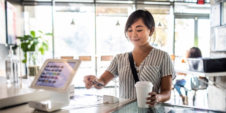 A person at the counter in a cafe uses a card to buy coffee.